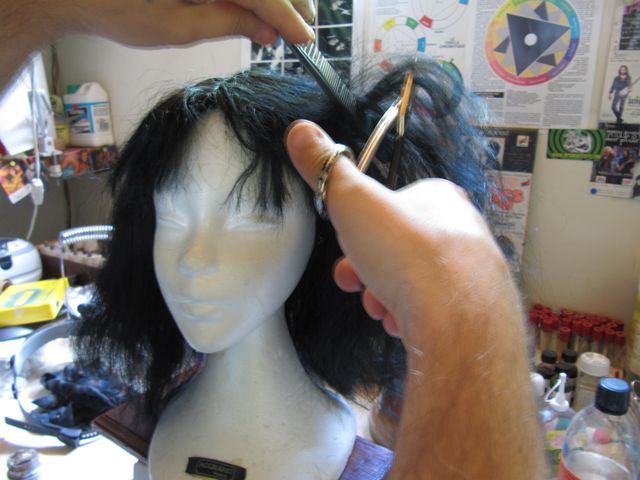 Découpe aux ciseaux et au peigne de la perruque brune installée sur une tête de mannequin