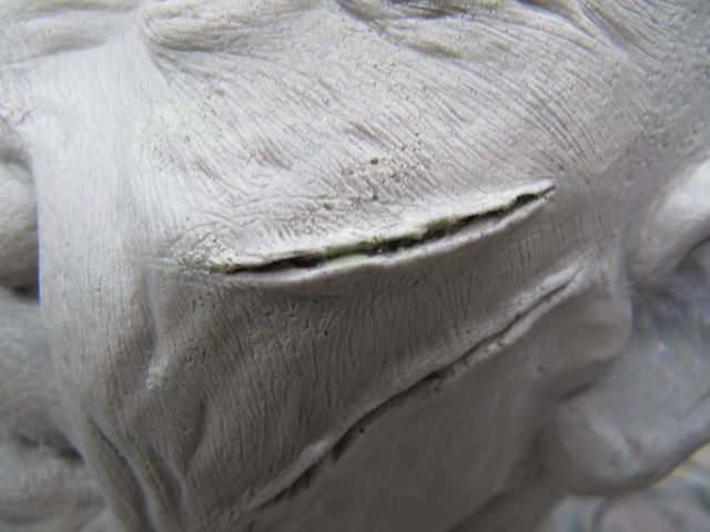 Gros plan sur le visage sculpté en mastic gris montrant rides et plaie texturées de Regan