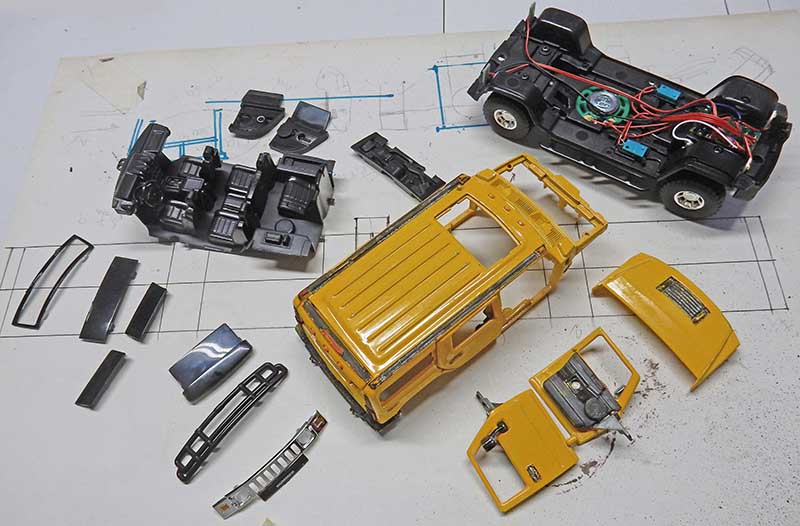 Pièces détachées d'une maquette de Hummer jaune en cours de montage avec châssis et câblage électrique
