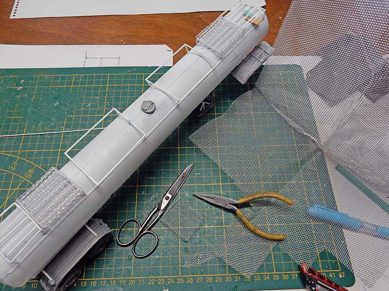 Maquette de camion-citerne gris en construction avec grillage métallique, ciseaux et pince sur tapis de découpe