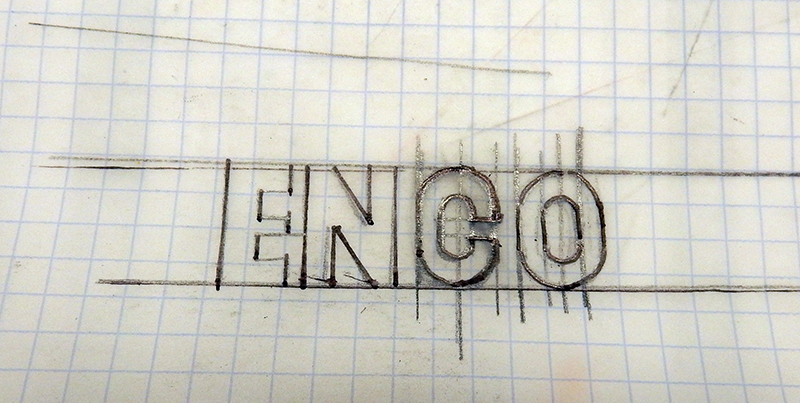 Croquis au crayon des lettres ENGO tracées sur papier millimétré pour reproduire un logo