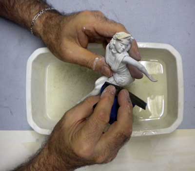 Ponçage humide d'une figurine de femme en résine au-dessus d'un bac d'eau