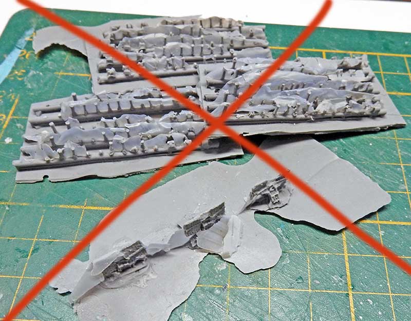 Pièces de maquette en résine grise barrées d'une croix rouge sur tapis de découpe