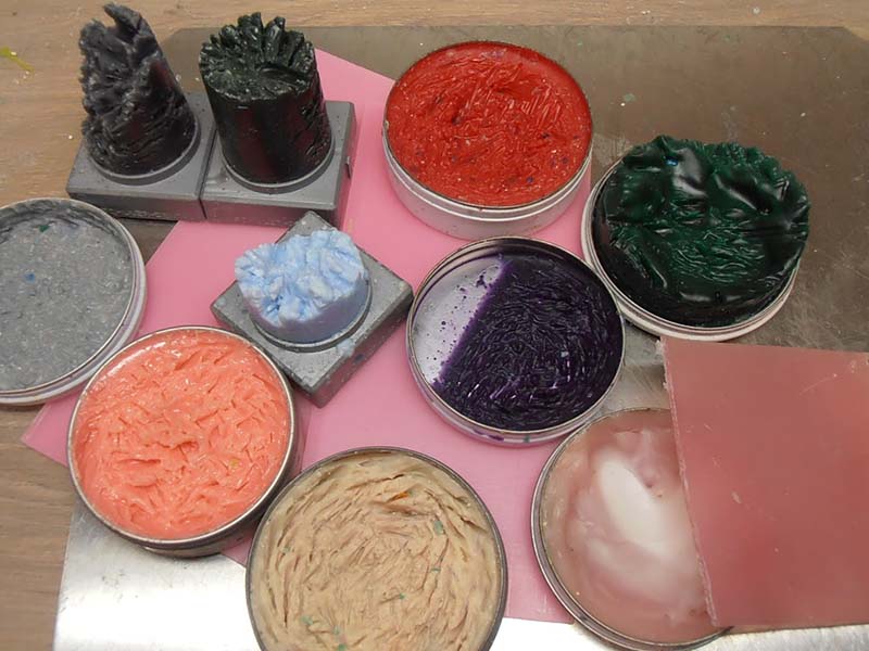 Cires de modelage de différentes couleurs dans des boîtes métalliques avec sculptures sur socles