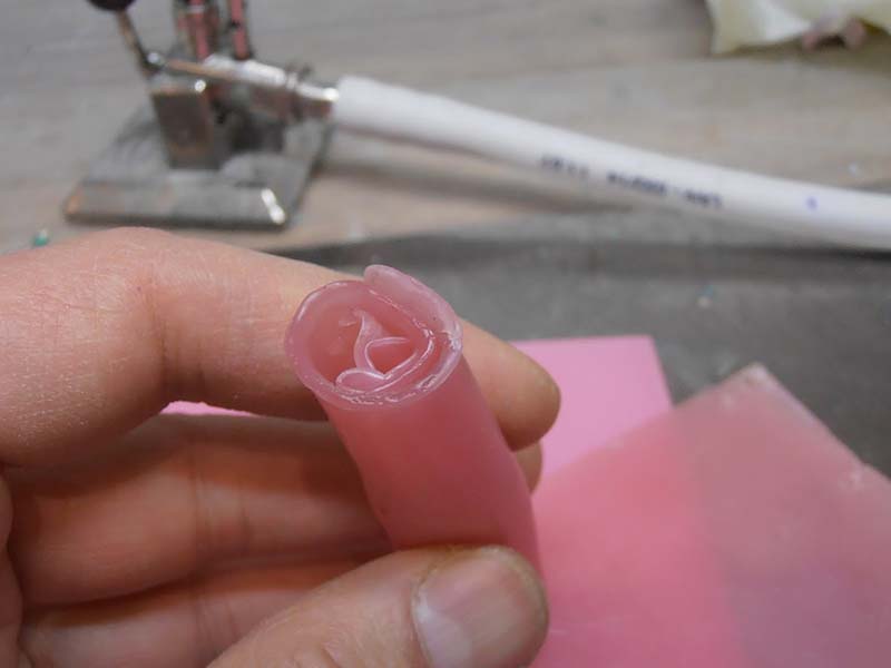 Doigts tenant une ébauche de cire rose translucide sculptée, outils et plaque de cire en arrière-plan