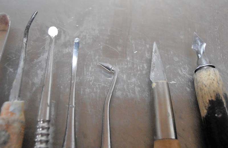 Outils métalliques de sculpture sur cire alignés mirettes lames et stylets sur surface grise