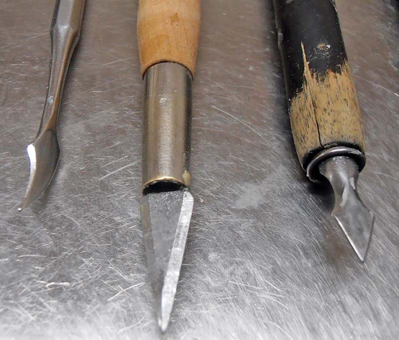 Trois outils de sculpture à pointes métalliques et manches en bois posés sur une surface métallique