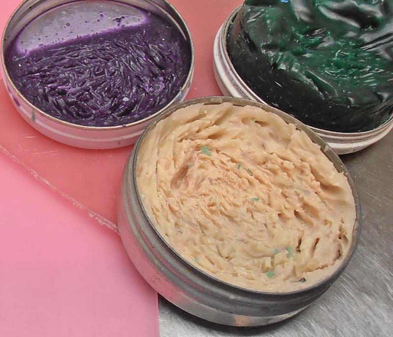 Trois boîtes métalliques de cire à sculpter violette, verte et beige sur un plan de travail