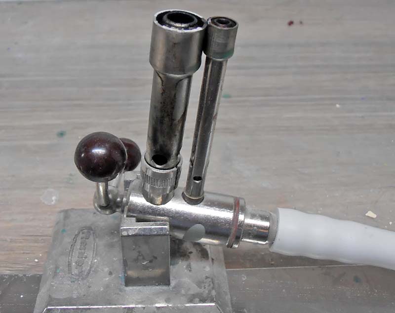 Stylo à cire électrique chromé sur socle métallique avec tuyau d'alimentation, posé sur établi