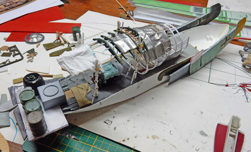 Maquette de bateau en construction sur un établi entourée de pièces, outils et matériaux de modélisme