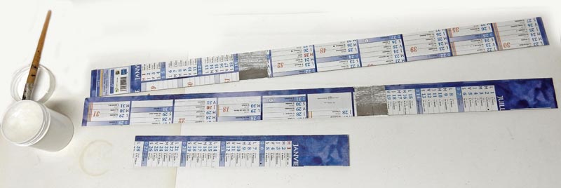 Bandes de papier imprimées bleues découpées pour maquette, posées près d'un pinceau et d'un pot de colle