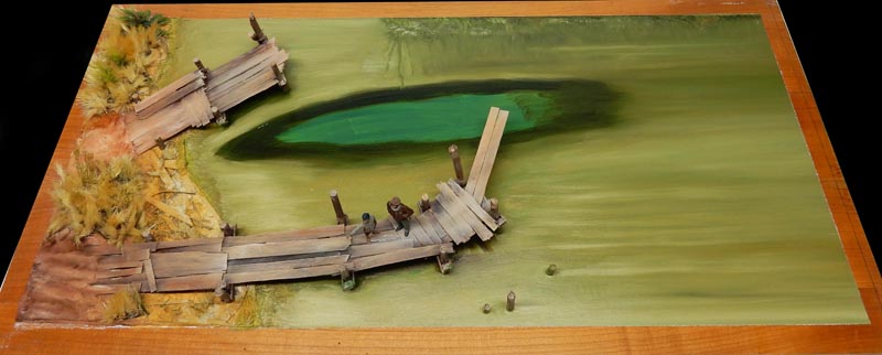 Maquette de diorama avec ponton en bois délabré longeant une rive marécageuse et deux figurines