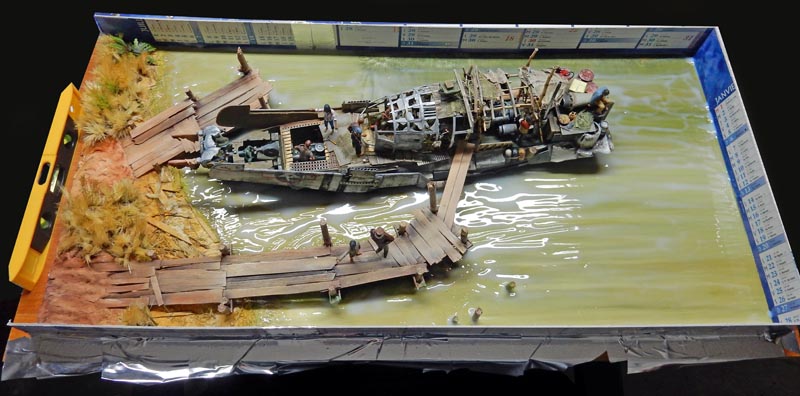 Diorama de maquettisme montrant une épave de bateau amarrée le long d'un ponton en bois
