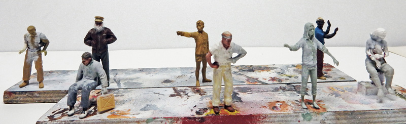Figurines de personnages peints à différents stades sur des socles maculés de peinture