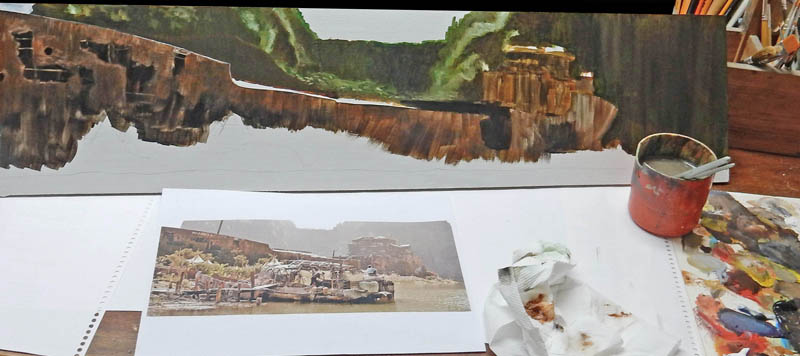 Décor peint de falaises en cours de réalisation avec photo de référence du village portuaire et godet de peinture