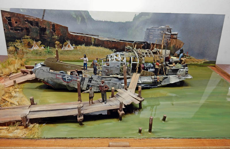 Diorama de maquettisme avec bateau délabré, pontons en bois et figurines sur eau verdâtre