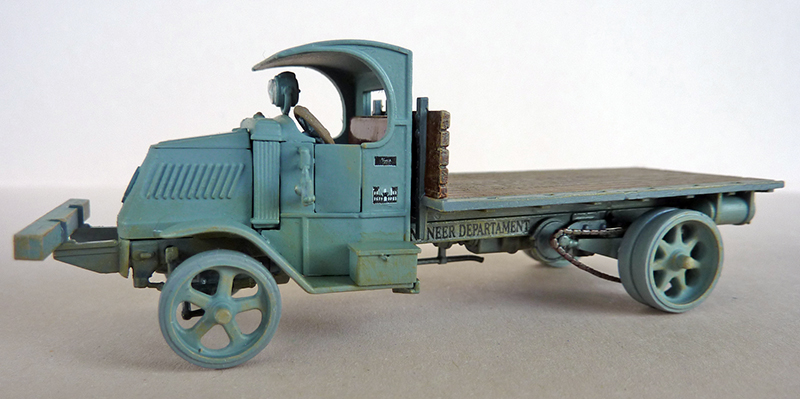 Maquette de camion plateau militaire vert avec conducteur, vue de profil sur fond neutre