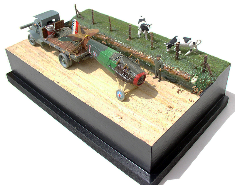 Diorama d'un biplan Spad accidenté remorqué par un camion, près d'un pré avec vaches