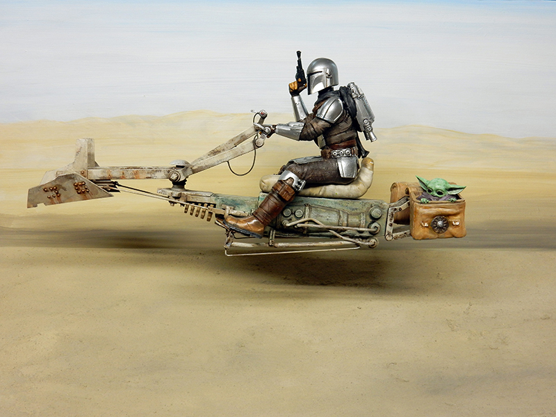 Diorama d'un guerrier mandalorien pilotant un speedbike au-dessus du désert, enfant vert embarqué
