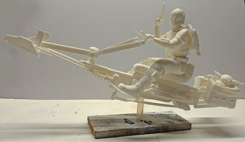 Maquette non peinte du speedbike Mandalorien avec pilote et enfant, montée sur socle