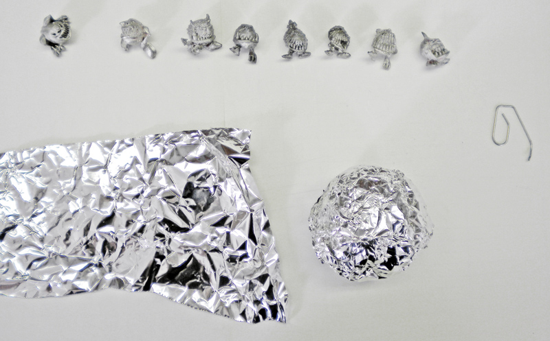 Huit figurines de Squig miniatures alignées au-dessus d'une feuille et d'une boule de papier aluminium