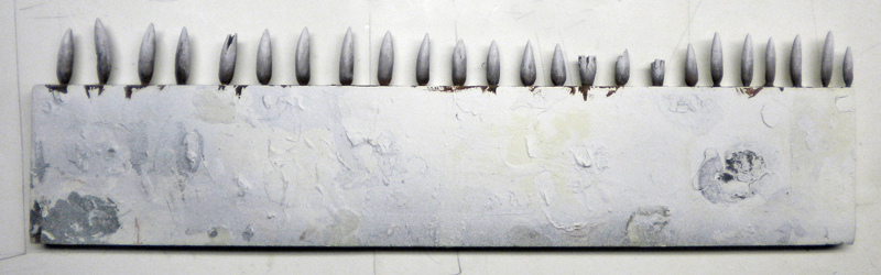 Rangée de dents pointues sculptées et peintes en gris sur une mâchoire de Squig