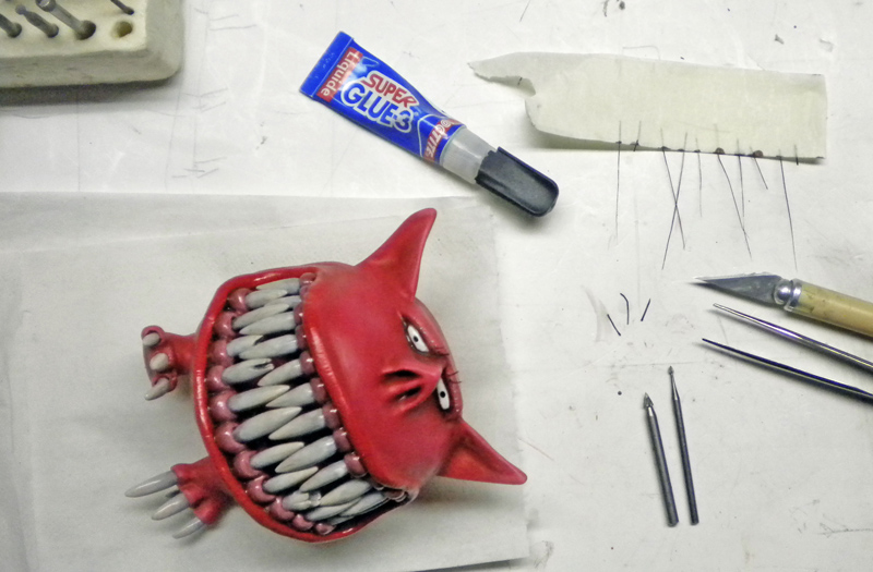 Squig rouge sculpté aux grandes dents sur plan de travail avec colle et outils