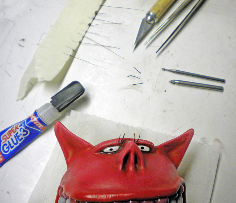 Tête de Squig rouge peinte à côté de colle, scalpel et fins poils à coller