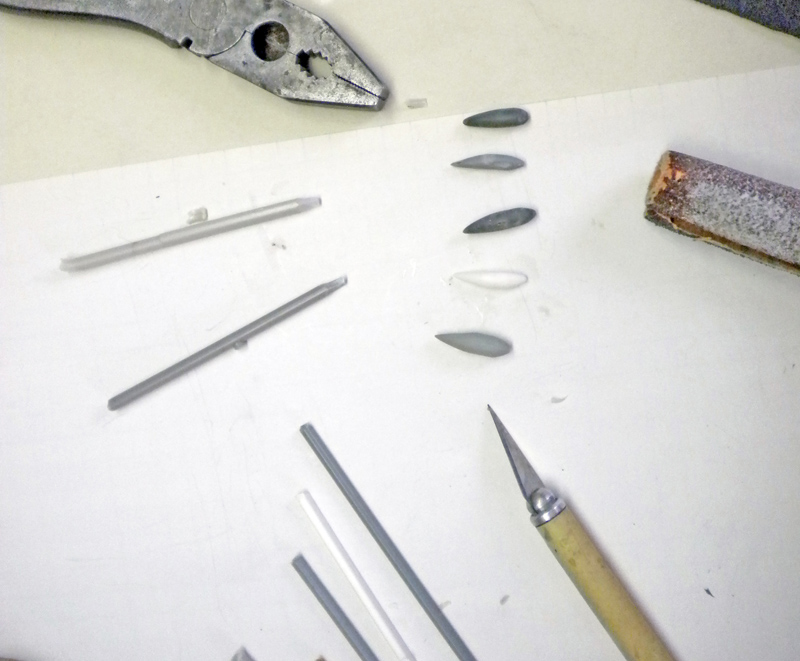 Pince, lime et scalpel autour de petites dents sculptées et tiges plastiques pour le Squig