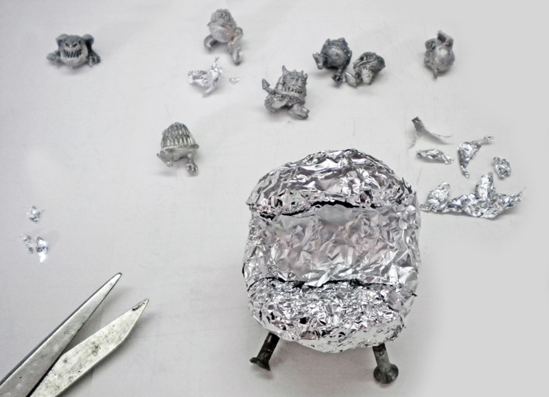 Structure d'un Squig en papier aluminium entourée de figurines miniatures et de ciseaux