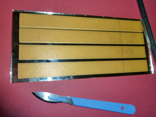 Découpe de bandes de balsa annotées sous une règle métallique, scalpel à côté