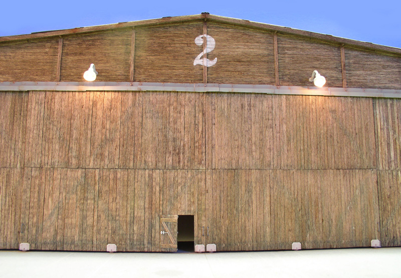Façade en bois du hangar numéro 2, porte entrouverte et lampes allumées au crépuscule