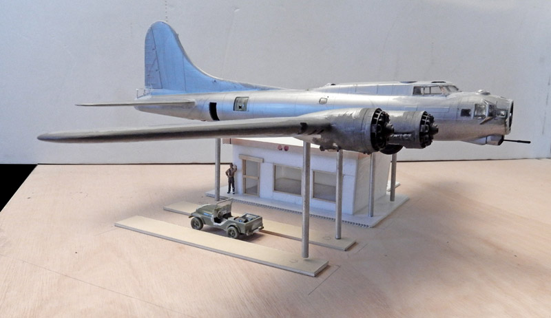 Maquette de bombardier quadrimoteur argenté monté sur pylônes au-dessus d'un bâtiment avec véhicule militaire
