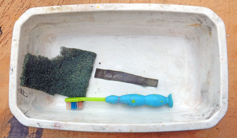 Brosse à dents bleue, tampon abrasif et bande métallique dans une coupelle en céramique blanche