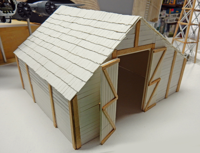 Maquette de hangar en bois clair aux portes ouvertes, avec toit en bardeaux blancs