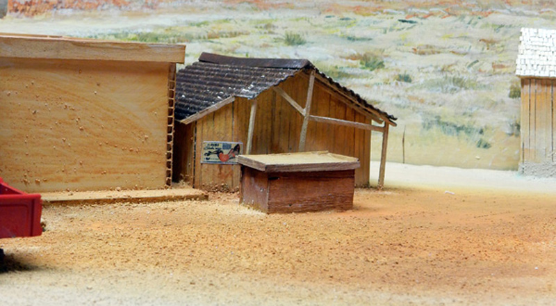 Maquette de hangars en bois sur sol désertique sablonneux avec décor de collines