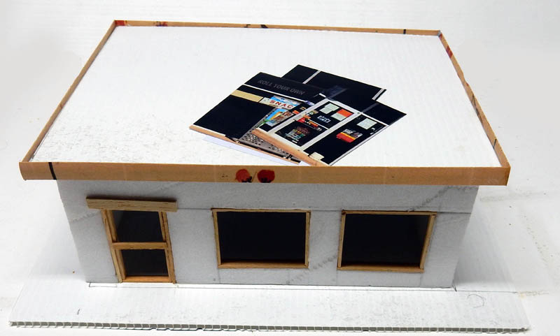 Maquette de bâtiment en carton avec fenêtres et photo de façade posée sur le toit