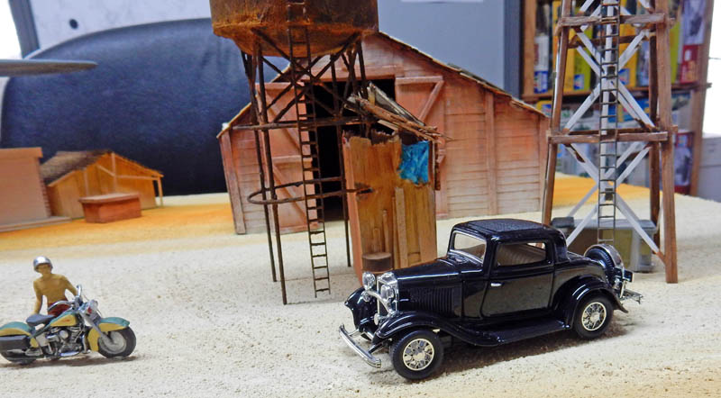 Maquette d'un coupé hot rod noir et d'une moto devant une grange et un château d'eau