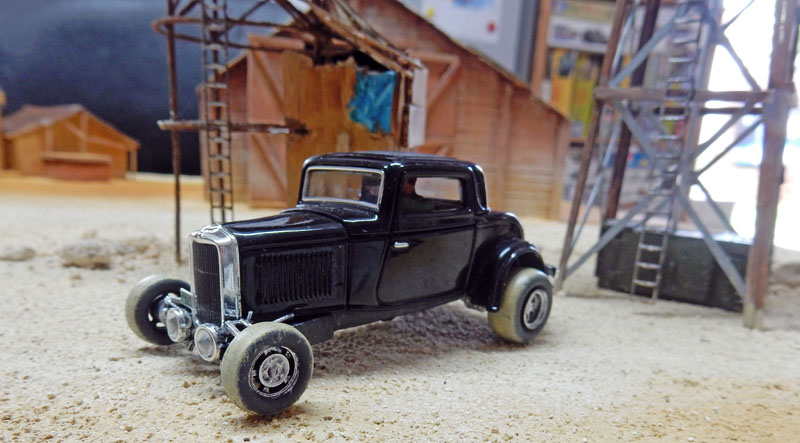 Maquette de hot rod noir devant un décor de hangar et château d'eau