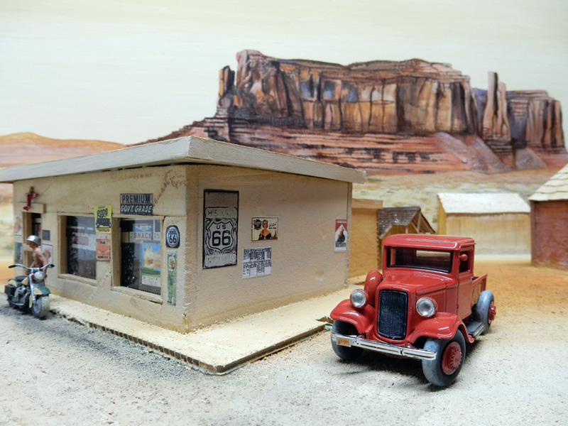 Maquette de station-service Route 66 avec camionnette rouge ancienne devant un décor désertique de mesa