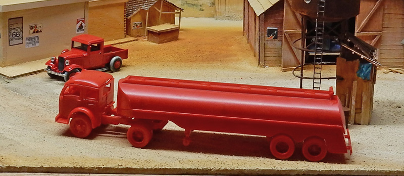 Maquettes de camion-citerne rouge et pick-up rouge sur diorama de gare western