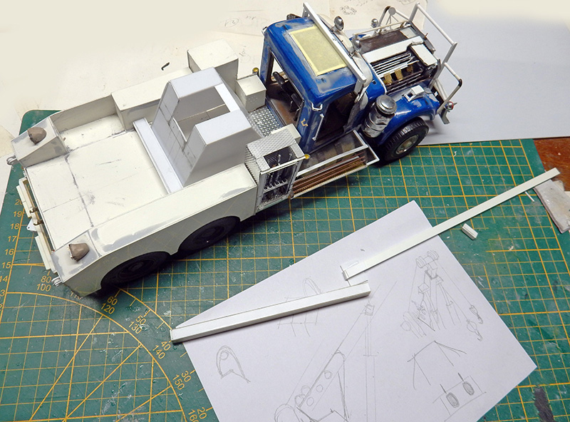 Maquette de dépanneuse à cabine bleue en construction sur tapis de découpe avec croquis préparatoires