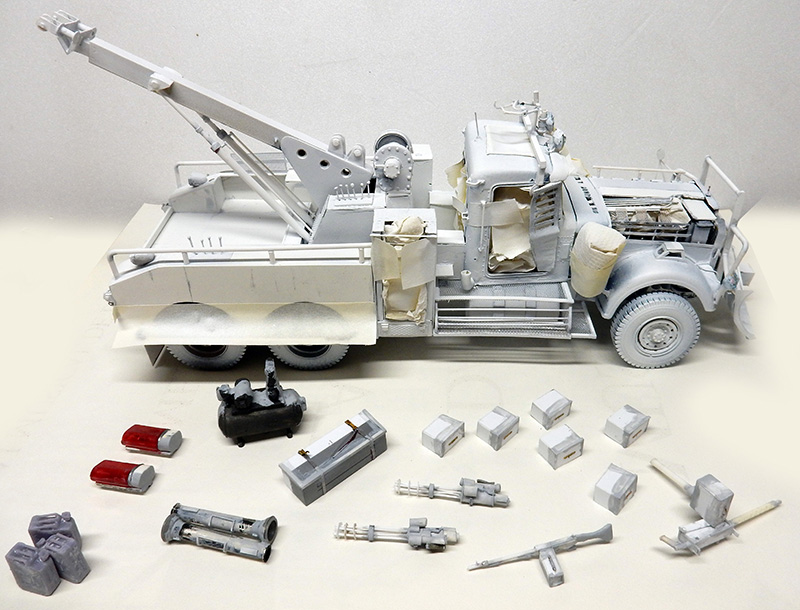 Maquette de dépanneuse avec grue entourée d'accessoires, caisses et armes en cours d'assemblage