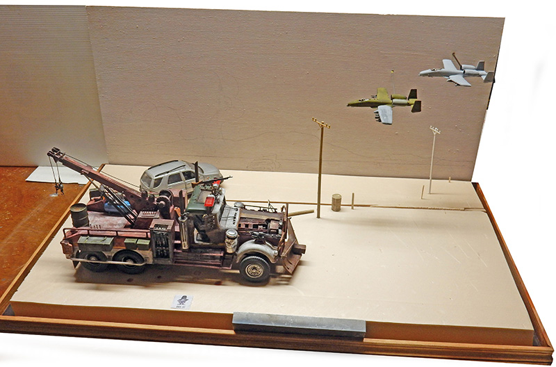 Maquette de dépanneuse blindée sur diorama avec deux avions de chasse en arrière-plan