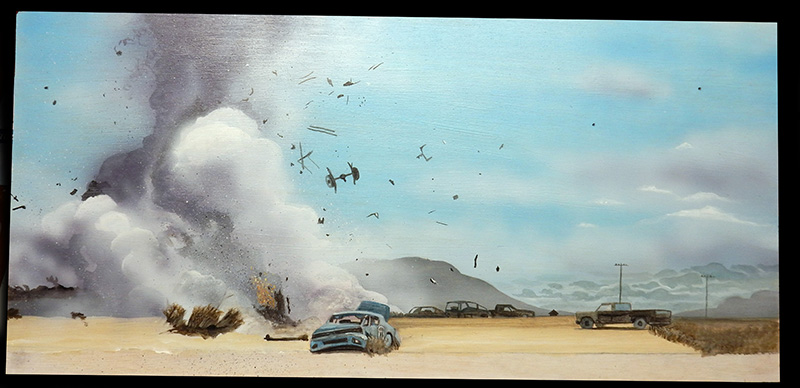 Décor désertique peint avec explosion, débris projetés, épaves de voitures et dépanneuse sous ciel bleu