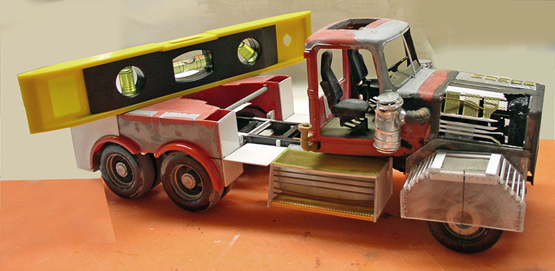 Maquette en carton d'une dépanneuse rouge usée posée sur un grand niveau à bulle jaune