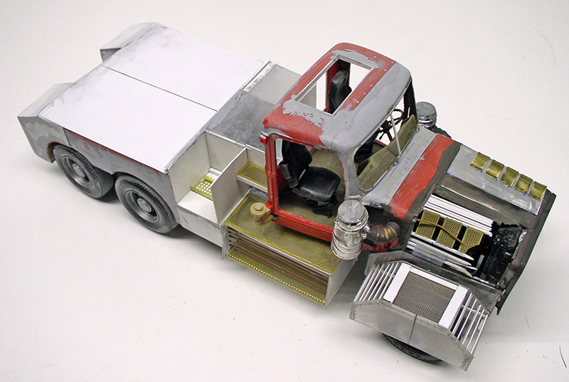 Maquette de camion dépanneuse en construction, cabine rouge et carrosserie métal vue trois quarts