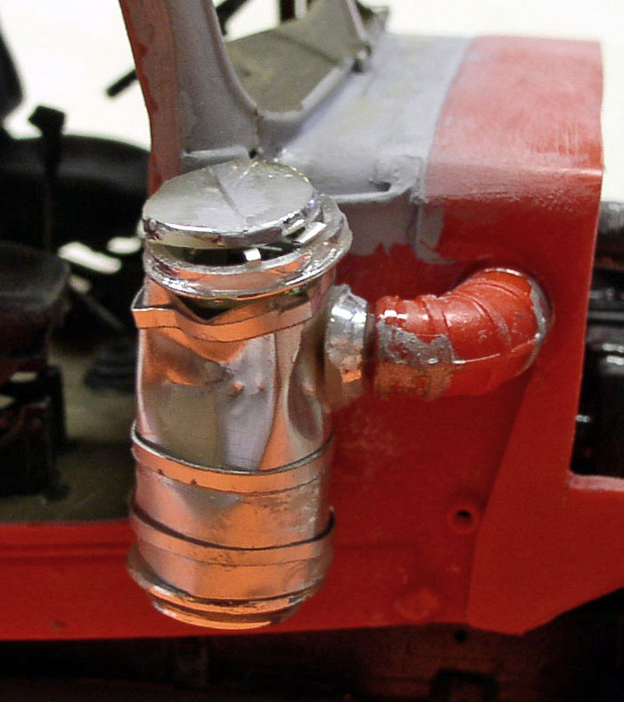 Détail d'un réservoir cylindrique métallique avec raccord coudé orange sur châssis rouge de maquette