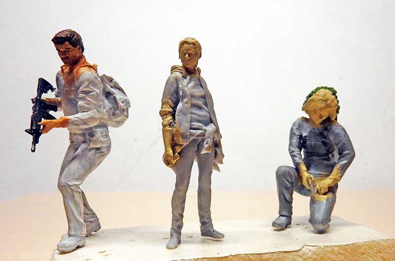 Trois figurines de personnages sculptés en cours de modelage, dont un armé d'un fusil