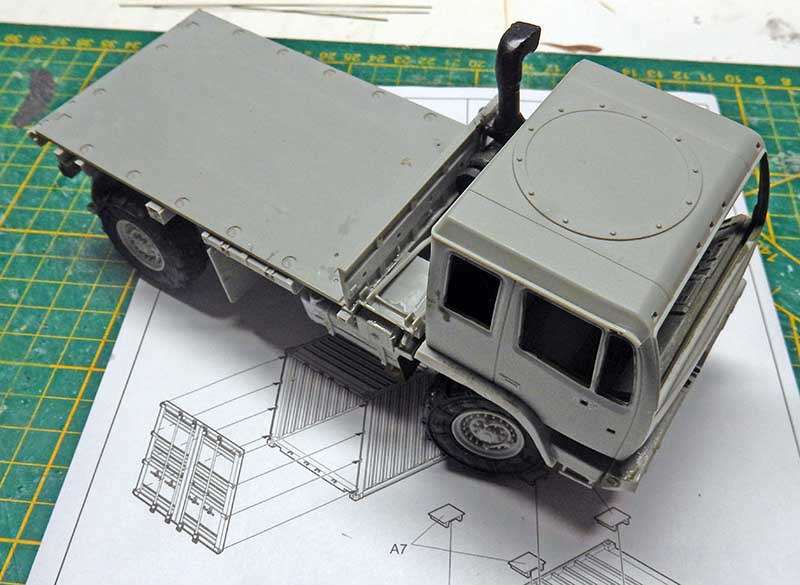 Maquette de camion plateau militaire en montage gris posée sur tapis de découpe avec plan